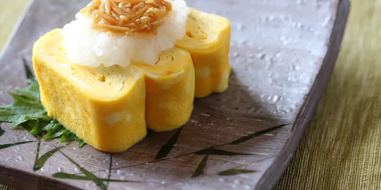 Roladki tamago z tartą rzodkwią i grzybami enoki na talerzu z motywem bambusa.