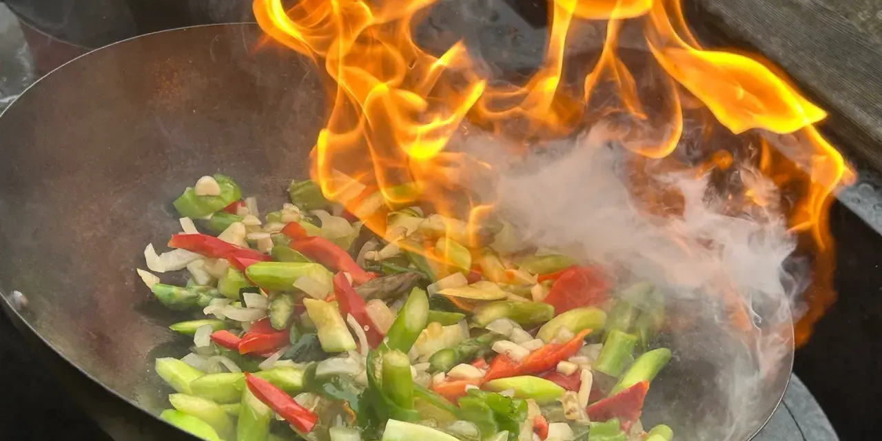 Ogień płonie w woku, przygotowując warzywa do stir fry. To szybkie smażenie, które zachowuje świeżość składników.
