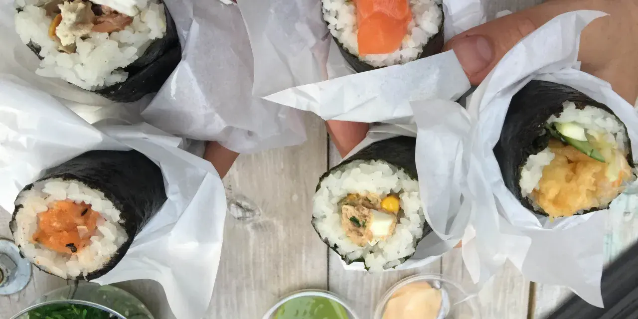 Ręcznie robione handroll sushi z łososiem, awokado, tuńczykiem i krewetkami. Pyszne przekąski na drewnianym stole.