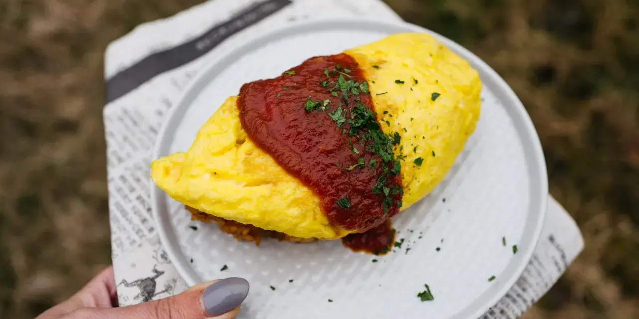 Pyszny omlet ryżowy polany sosem pomidorowym i posypany natką pietruszki, podany na talerzu.
