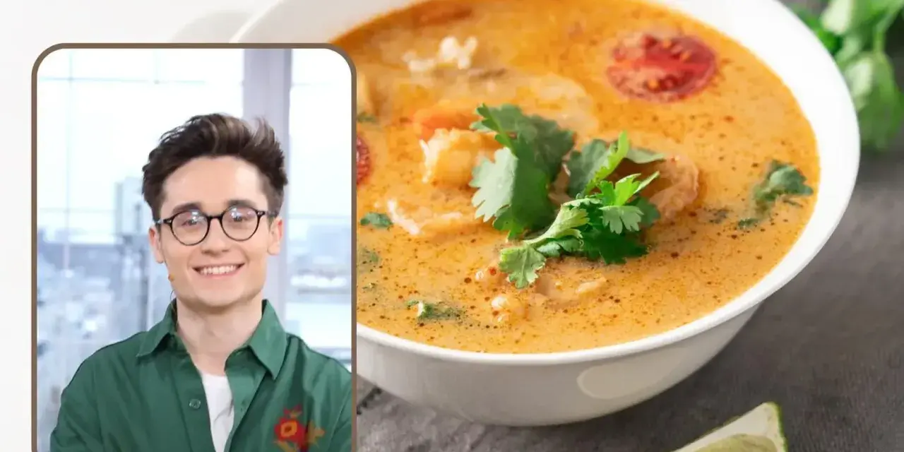 Uśmiechnięty mężczyzna w okularach prezentuje aromatyczną zupę tajską z krewetkami i pomidorkami, ozdobioną świeżą kolendrą.
