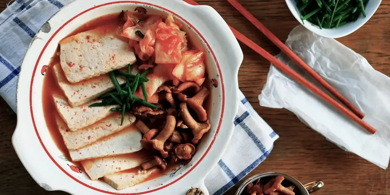 Pyszne kimchi jjigae z tofu i grzybami, podane z zieloną cebulką.