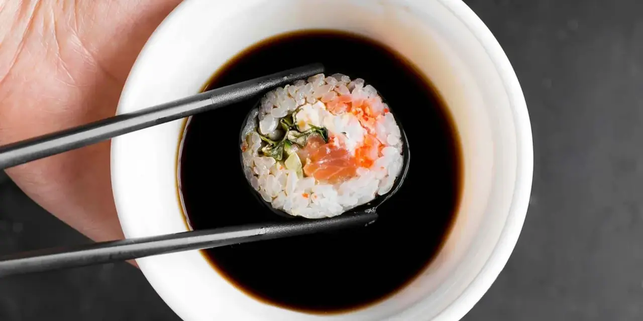 Pałeczkami zanurzam rolkę sushi w ciemnym sosie. Idealny sos słodki do sushi podkreśla smak ryby i ryżu.