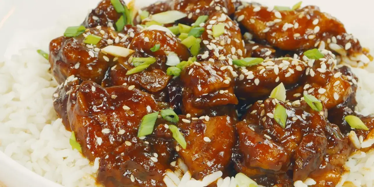Pyszny kurczak Tso w sosie, posypany sezamem i szczypiorkiem, podany na ryżu.
