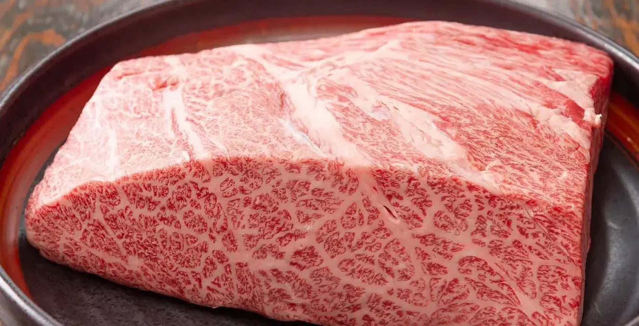 Wyjątkowy kawałek wołowiny wagyu z widocznym marmurkowym przerostem tłuszczu, prezentowany na ciemnej tacy.