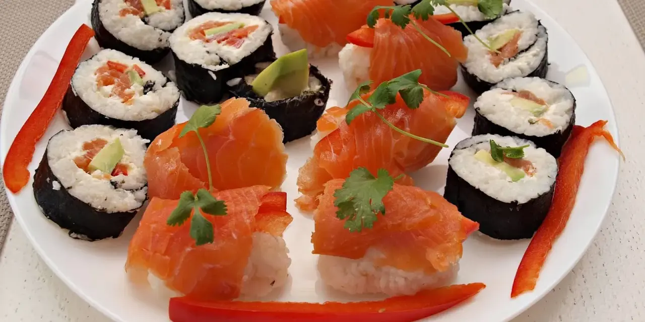Piękne sushi kompozycje na białym talerzu: rolki z łososiem, awokado i papryką, ozdobione kolendrą.