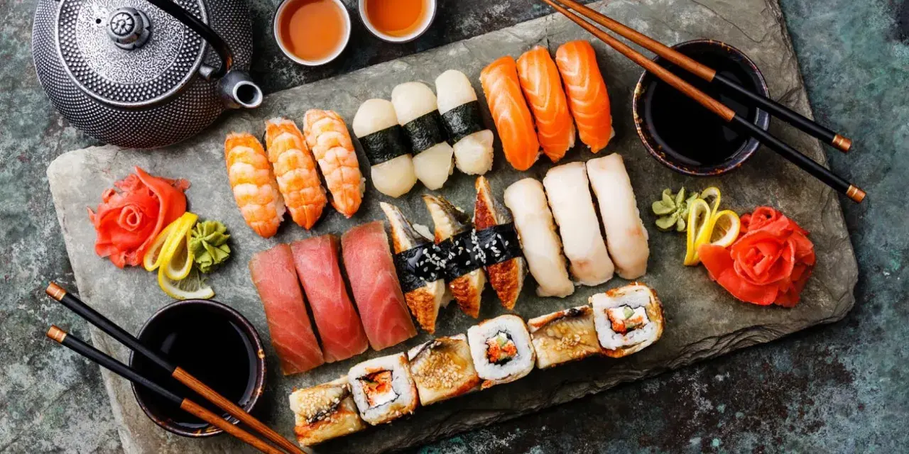 Zestaw sushi: nigiri z łososiem, krewetkami, tuńczykiem, węgorzem i rolki. Obok czajniczek, miseczki z herbatą i sos sojowy. Tak jedzą japończycy.
