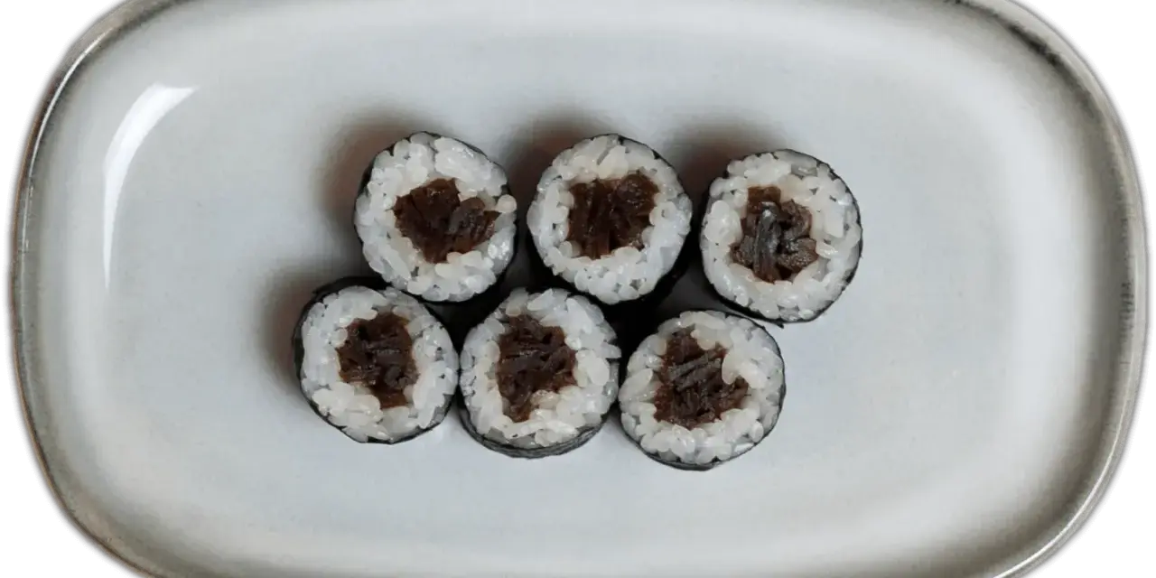 Sześć kawałków sushi z ryżem i ciemnym nadzieniem na szarej tacy.