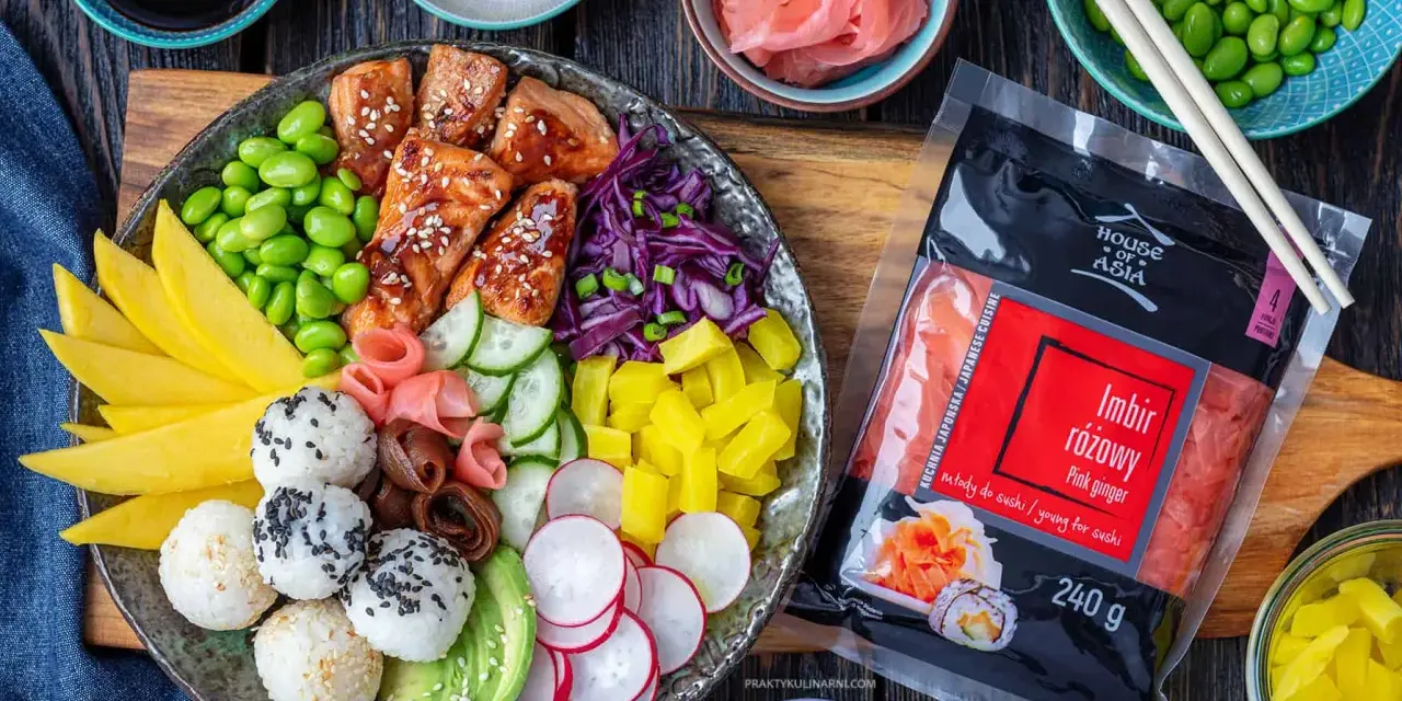 Kolorowy bowl z kawałkami glazurowanego lososia, ryżem, awokado, mango, ogórkiem, rzodkiewką, edamame i marynowanym imbirem. Obok opakowanie różowego imbiru.