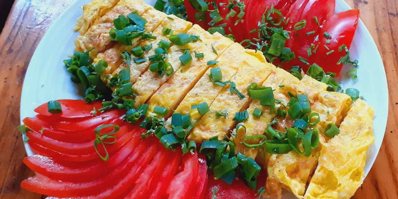 Pyszne koreańskie śniadanie: pokrojony omlet z jajek posypany szczypiorkiem, podany z plasterkami pomidora.