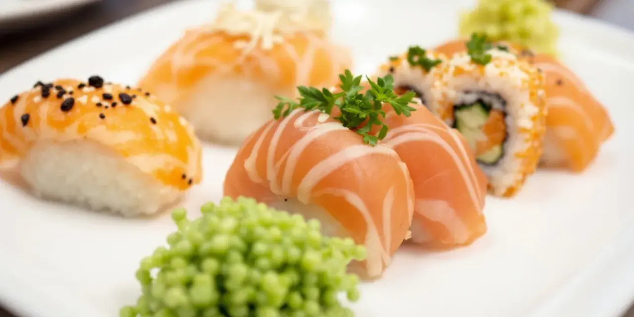 Talerz z różnorodnym nigiri sushi z łososiem, posypane sezamem i ozdobione natką pietruszki. Obok porcja zielonego wasabi.