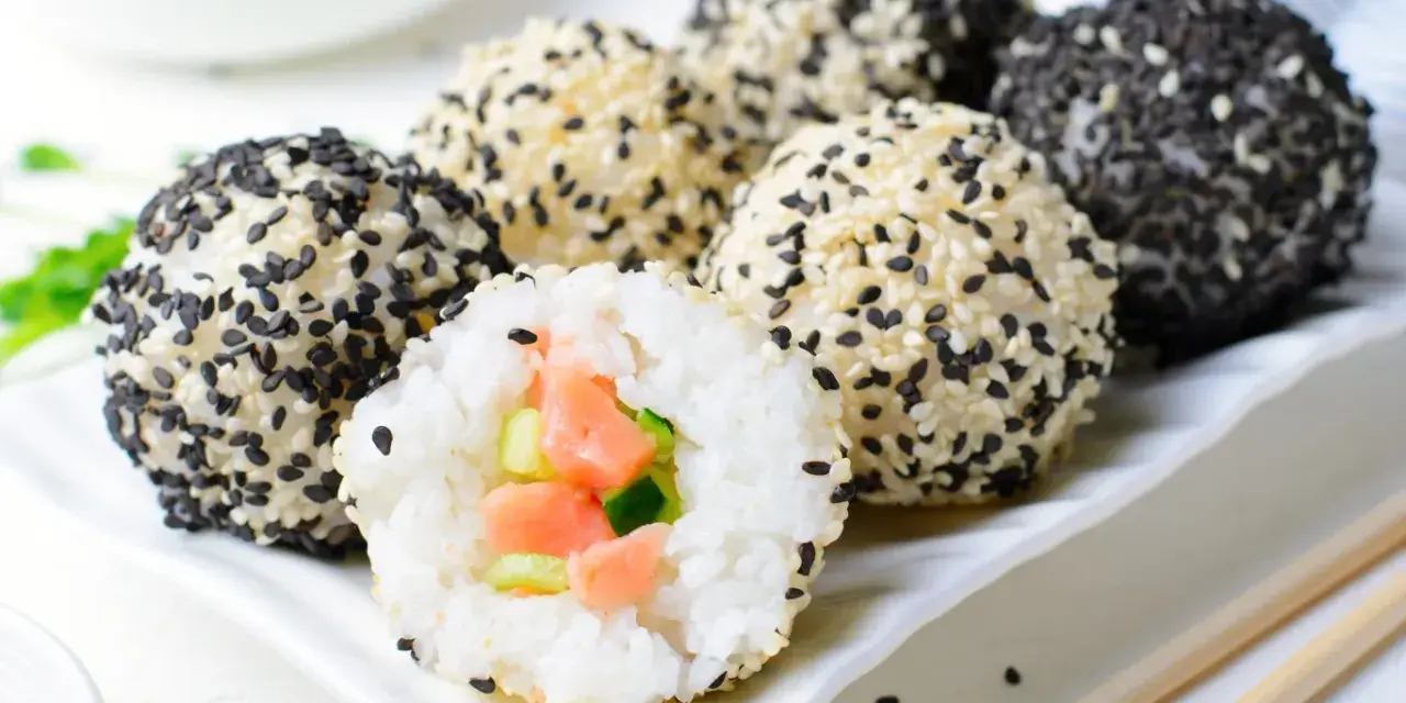 Szybkie sushi w kulkach, obtoczone białym i czarnym sezamem. Jedna kulka jest przekrojona, ukazując łososia i ogórek.