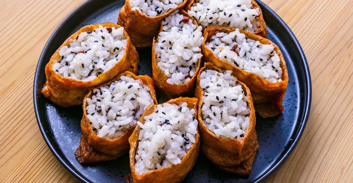 Tofu inari z ryżem i czarnym sezamem na czarnym talerzu.