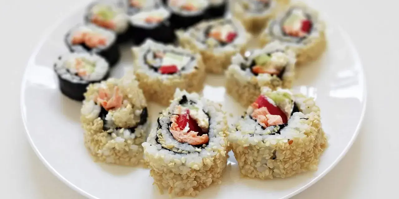 Talerz pełen sushi uramaki z łososiem, awokado i papryką, posypane sezamem. Pyszne i kolorowe rolki.