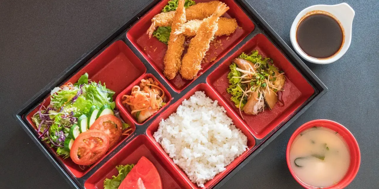Japoński obiad w bento: smażone krewetki, ryż, sałatka, owoce i zupa miso.