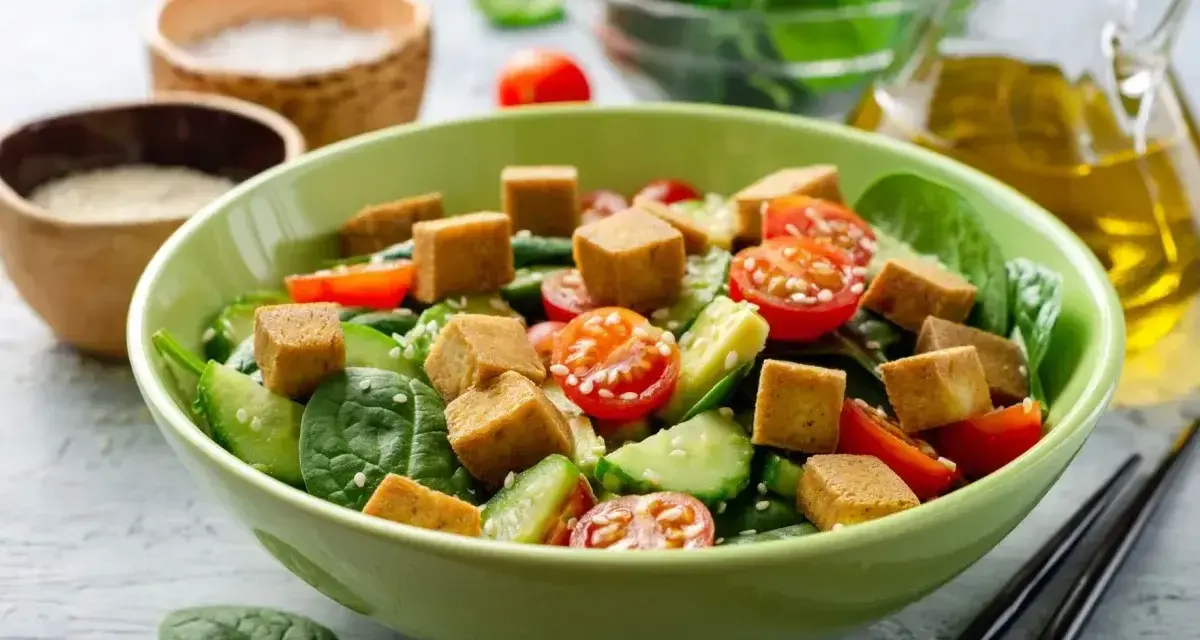 Sałatka ze szpinakiem, pomidorkami, ogórkiem i kostkami **butter tofu**, posypana sezamem.