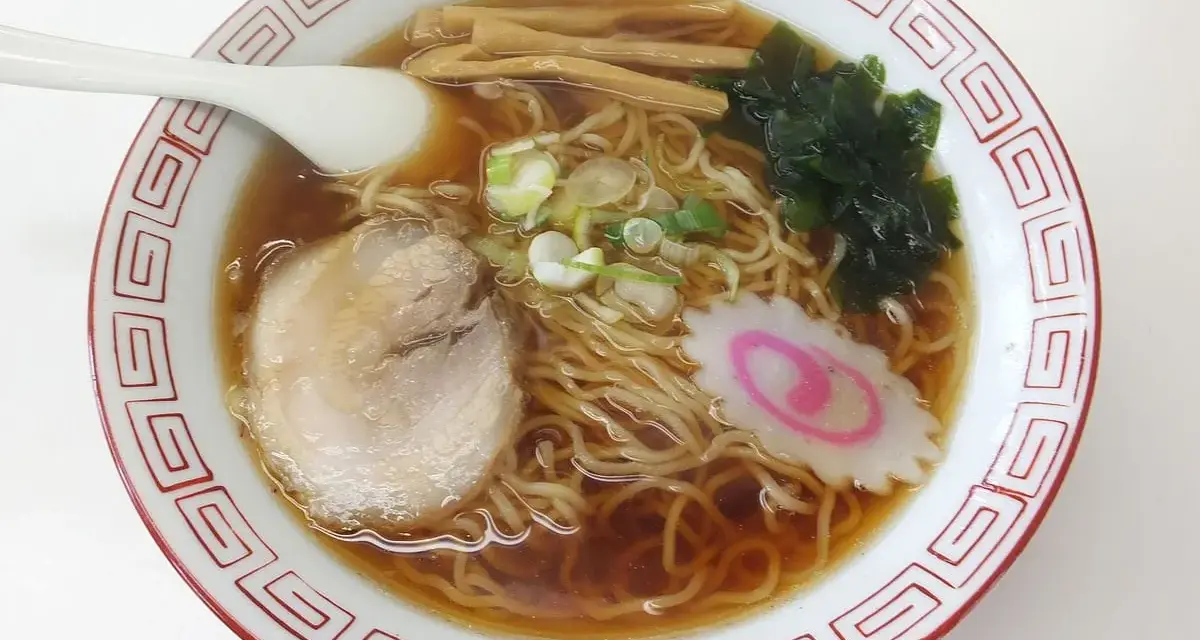 Miseczka aromatycznego ramenu, dania, którego **ramen skąd pochodzi** jest z Japonii. Widać makaron, plastry mięsa, nori, bambus i narutomaki.