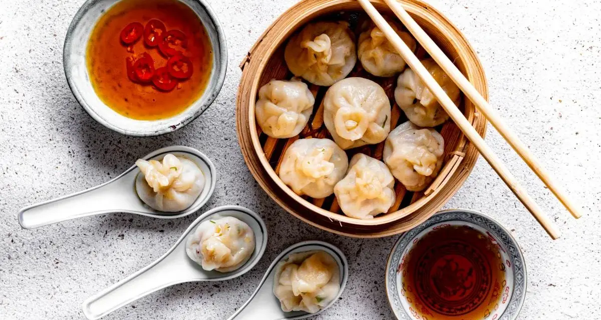 Pyszne dim sum w bambusowym parowniku, podane z sosem chili i sosem sojowym. Trzy pierożki na łyżeczkach zachęcają do spróbowania.