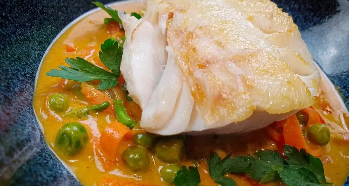 Aromatyczny curry z dorszem, podane z groszkiem i marchewką w kremowym sosie.