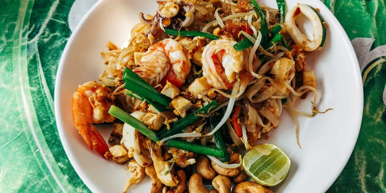 Pad thai z krewetkami, kalmarami, kiełkami i orzechami nerkowca. Widać też kawałek limonki, idealne pad thai składniki.
