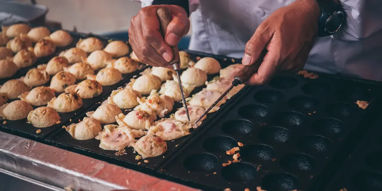 Ręce obracają kulki takoyaki na specjalnej patelni. Ten prosty takoyaki przepis jest w trakcie realizacji.