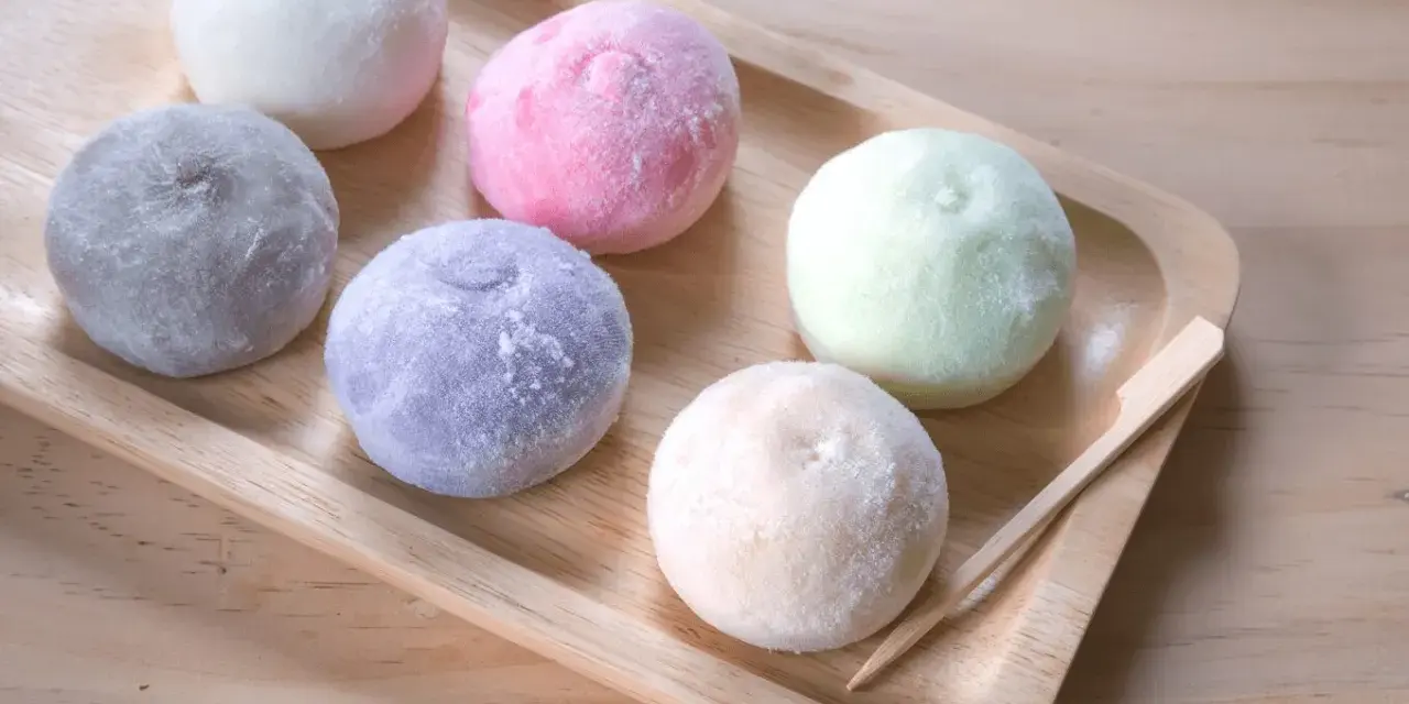 Kolorowe desery azjatyckie, mochi, ułożone na drewnianej tacy.
