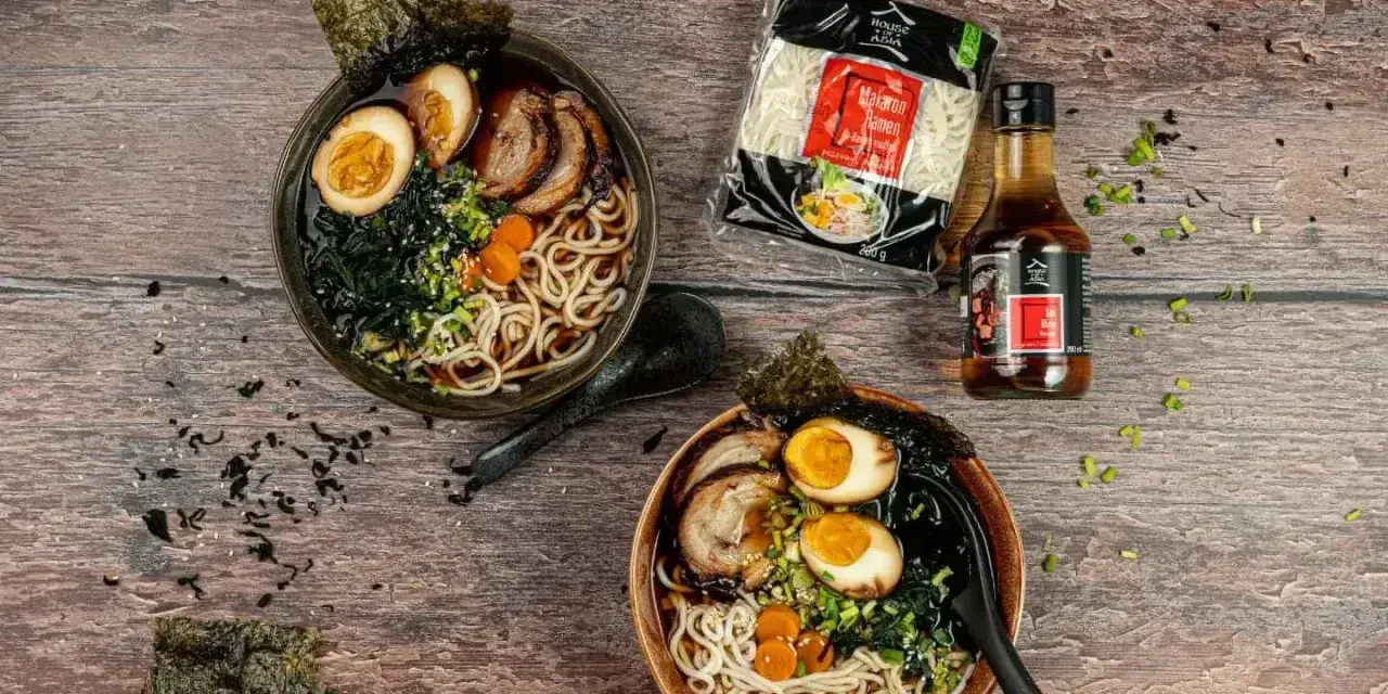Dwie miski aromatycznego makaronu ramen z sosem sojowym, jajkiem, mięsem i wodorostami. Obok opakowanie makaronu i butelka sosu.
