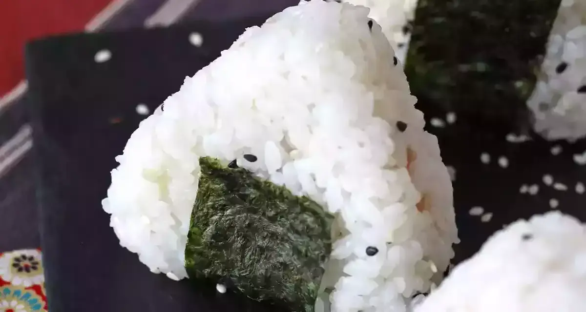 Trójkątne onigiri z tuńczykiem, ryżem i wodorostami nori, posypane sezamem.