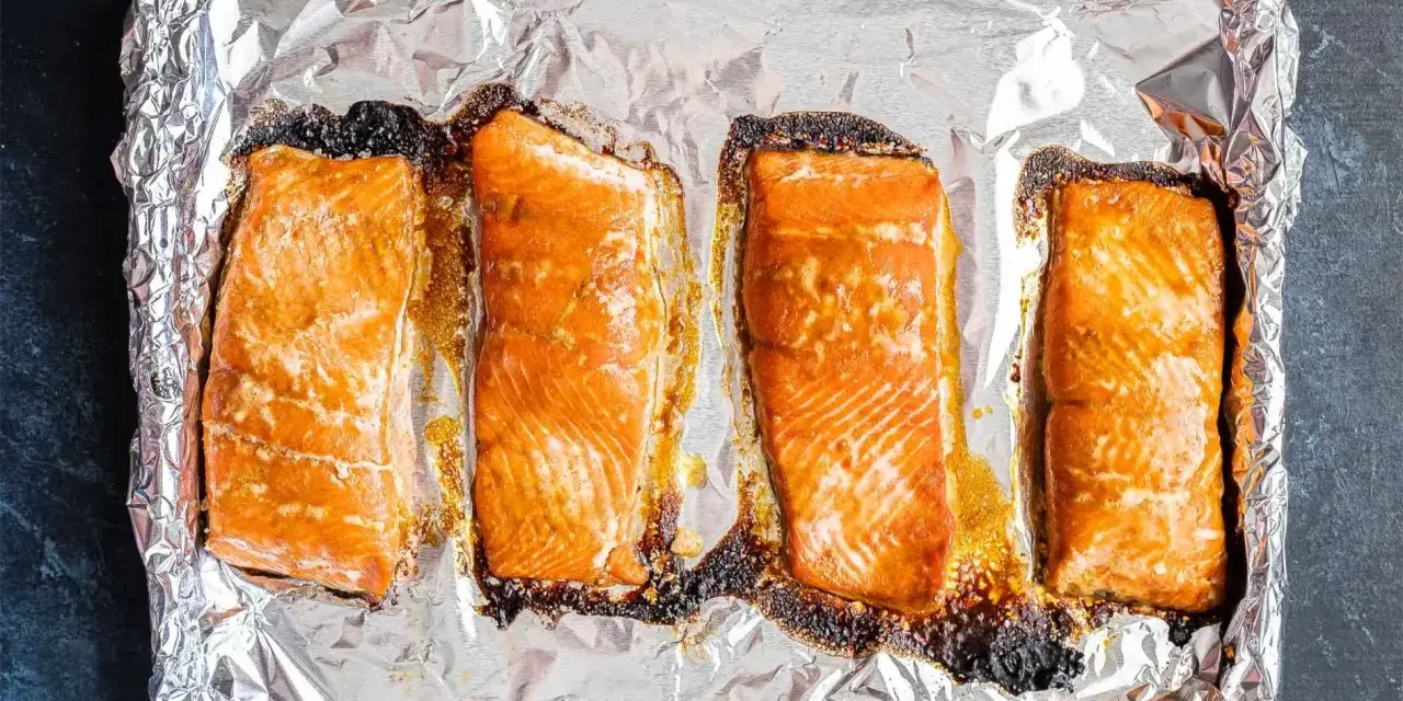 Cztery kawałki pieczonego łososia na folii aluminiowej. Idealny łosoś do sushi, lekko przypieczony na brzegach, zachęca do przygotowania.