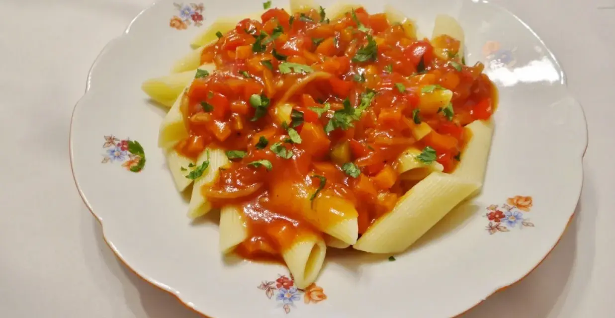 Penne z aromatycznym, słodko-kwaśnym sosem warzywnym, posypane świeżą natką pietruszki.