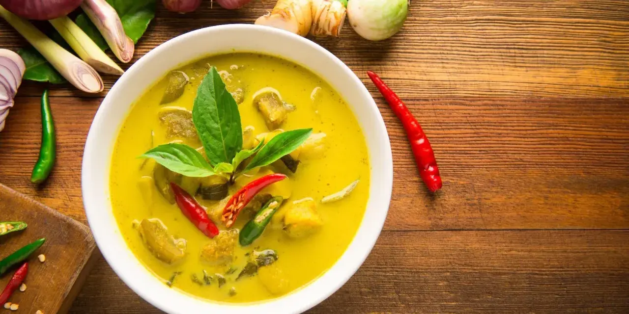 Aksamitne tajskie curry z tofu, ozdobione świeżą bazylią i papryczkami chili, otoczone składnikami jak galangal i trawa cytrynowa.