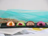 Cztery kolorowe mochi: pomarańczowe, zielone z malinami, czekoladowe i fioletowe z jagodami. Różne rodzaje słodkości.