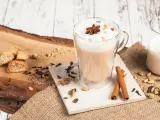 Aromatyczny napój, czyli chai, w szklance z pianką i anyżem. Obok cynamon, kardamon, goździki i ciasteczka.