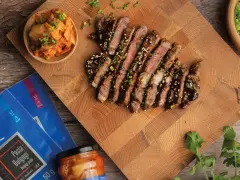 Pokrojony stek bulgogi polany sosem, obok miseczka z kimchi i opakowanie pasty do bulgogi.