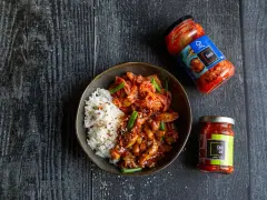 Miseczka ryżu z kurczakiem w sosie i kimchi, obok słoiczki z kimchi i pastą chili.