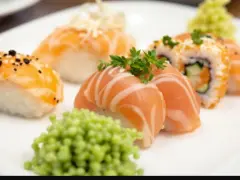 Talerz z różnorodnym nigiri sushi z łososiem, posypane sezamem i ozdobione natką pietruszki. Obok porcja zielonego wasabi.