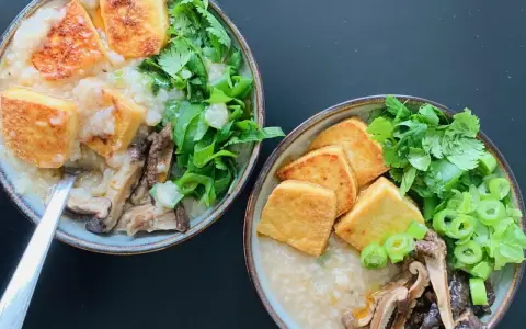 Dwie miseczki aromatycznego congee z chrupiącym tofu, grzybami i świeżymi ziołami.