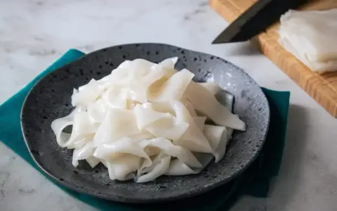 Płaski, biały makaron ryżowy na talerzu, gotowy do przygotowania pysznych dań. Szukasz inspiracji? Sprawdź makaron vermicelli przepisy!