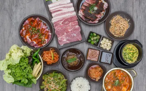 Obfity zestaw do korean bbq: surowe i marynowane mięso, kimchi, sałatki, ryż i dodatki.