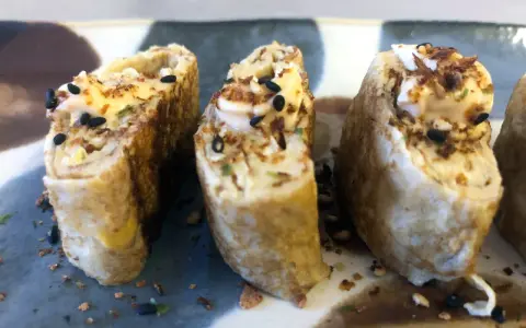 Trzy kawałki sushi w omlecie, polane majonezem i posypane czarnym sezamem.