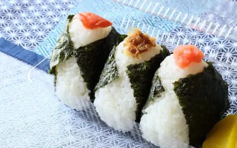 Trzy onigiri z ryżem, zawinięte w nori, z łososiem, tuńczykiem i ikrą na wierzchu. Idealne na przekąskę.