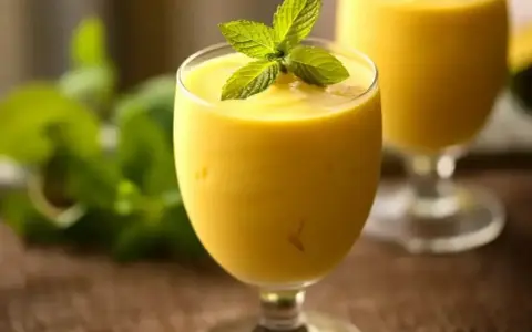 Orzeźwiający mango lassi z mlekiem kokosowym, ozdobiony listkiem mięty. Idealny na upalne dni.