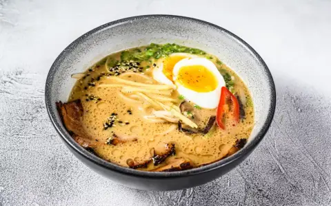 Miseczka aromatycznej zupy ramen z jajkiem na pół, plastrami mięsa, grzybami i szczypiorkiem.