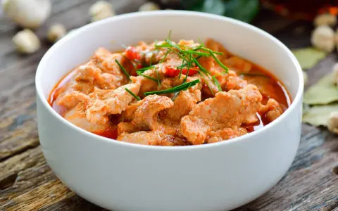 Pyszne wieprzowina w sosie curry, udekorowana szczypiorkiem i papryczką chili, podana w białej misce na drewnianym stole.