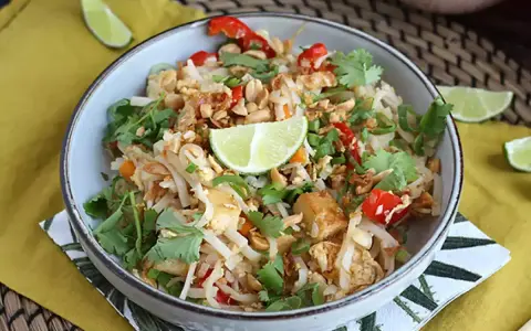 Pyszne pad thai z tofu, posypane orzeszkami ziemnymi i świeżą kolendrą, z kawałkami limonki.