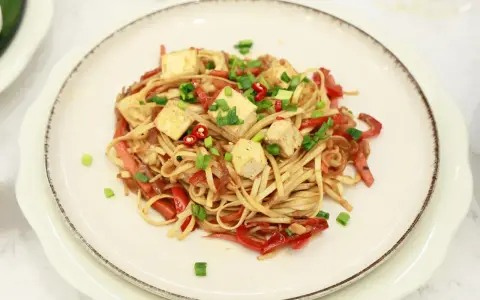 Smażony makaron Chow Mein z tofu, papryką i szczypiorkiem na talerzu.