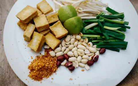 Składniki do pad ka prow: smażone kostki tofu, kiełki fasoli mung, szczypiorek, orzeszki ziemne, limonka i płatki chili.