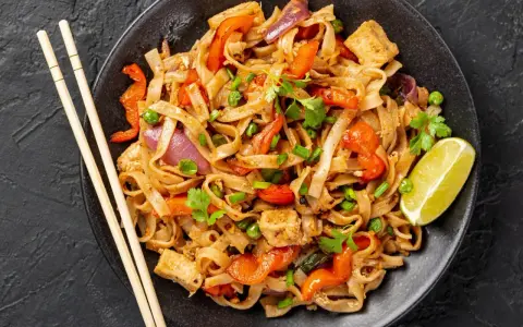 Talerz pełen Pad Thai: makaron ryżowy, tofu, papryka, cebula, groszek i kolendra. Idealny sposób, by dowiedzieć się, pad thai co to.