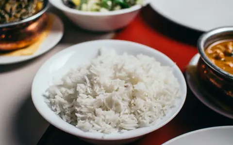 Biały ryż w misce, który jest głównym źródłem węglowodanów w wielu kuchniach. Obok dania curry i sałatka.