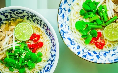 Dwie miseczki aromatycznej zupy pho z makaronem, mięsem, kiełkami, limonką, chili i świeżymi ziołami.